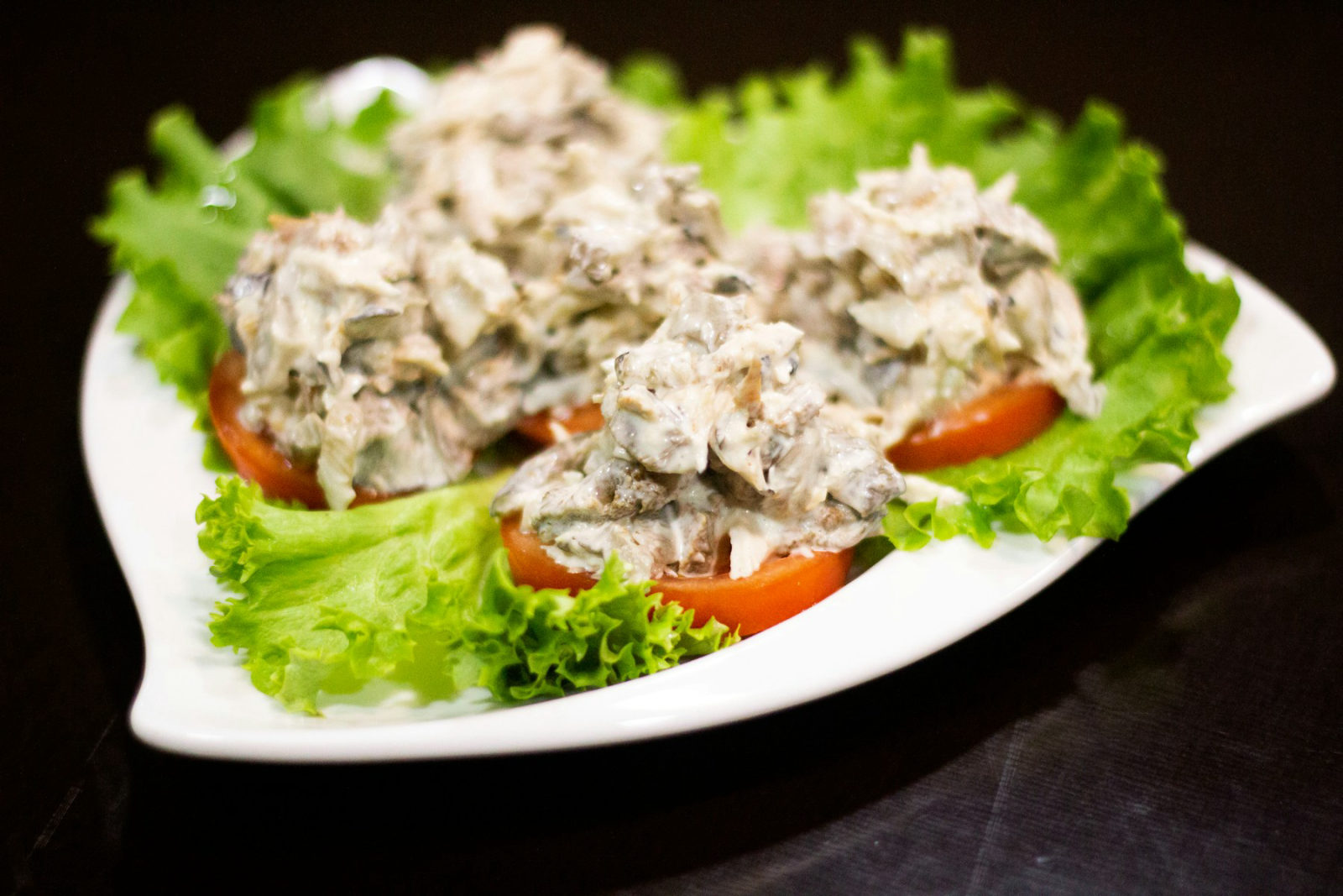 Cremiger Geflügelsalat mit Pilzen, auf Tomatenscheiben und Salatblättern angerichtet